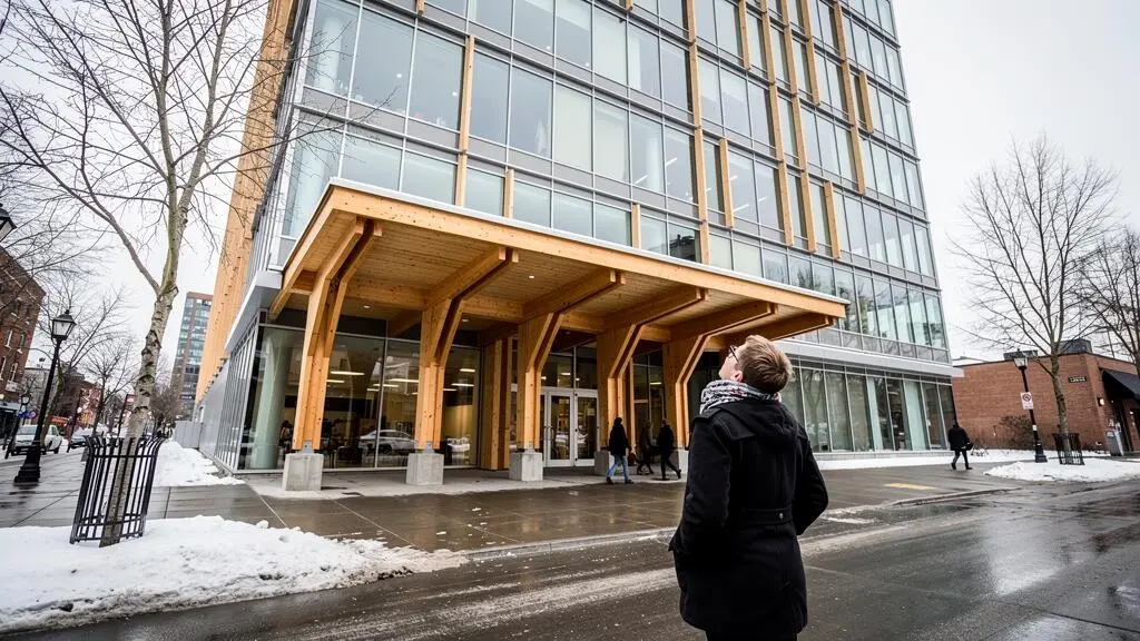 Passants devant un bâtiment contemporain canadien en bois lamellé-croisé et verre, sur un trottoir avec restes de neige en fin d'hiver.