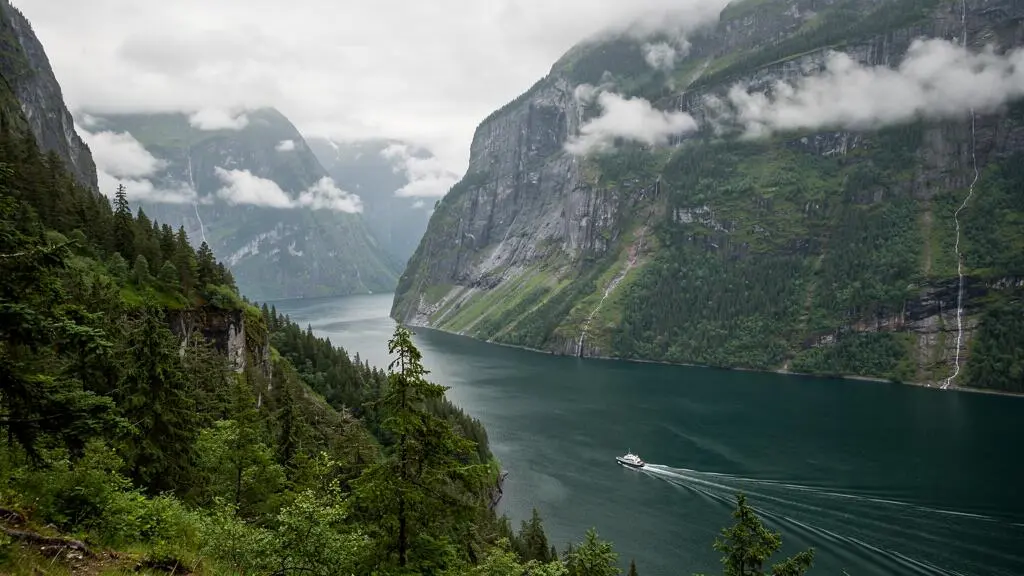 Fjord profond bordé de forêt pluviale tempérée sur la côte centrale de la Colombie-Britannique, avec un petit bateau traversant l'eau sous une lumière matinale voilée.
